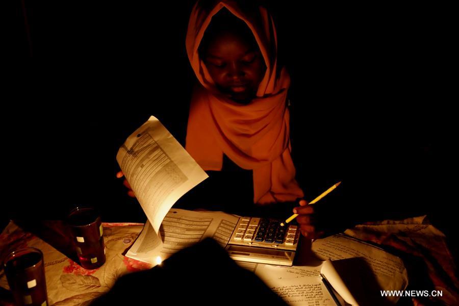 الصورة: طالبة سودانية تذاكر على ضوء شمعة عقب انقطاع التيار الكهربي 
