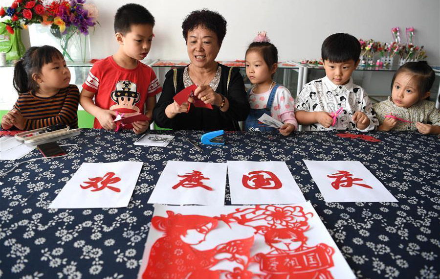 أطفال يتعلمون فن قص الورق الصيني التقليدي لاحتفال بالعيد الوطني